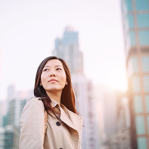 Young Asian woman looking up with smile on a bright morning against city skyline